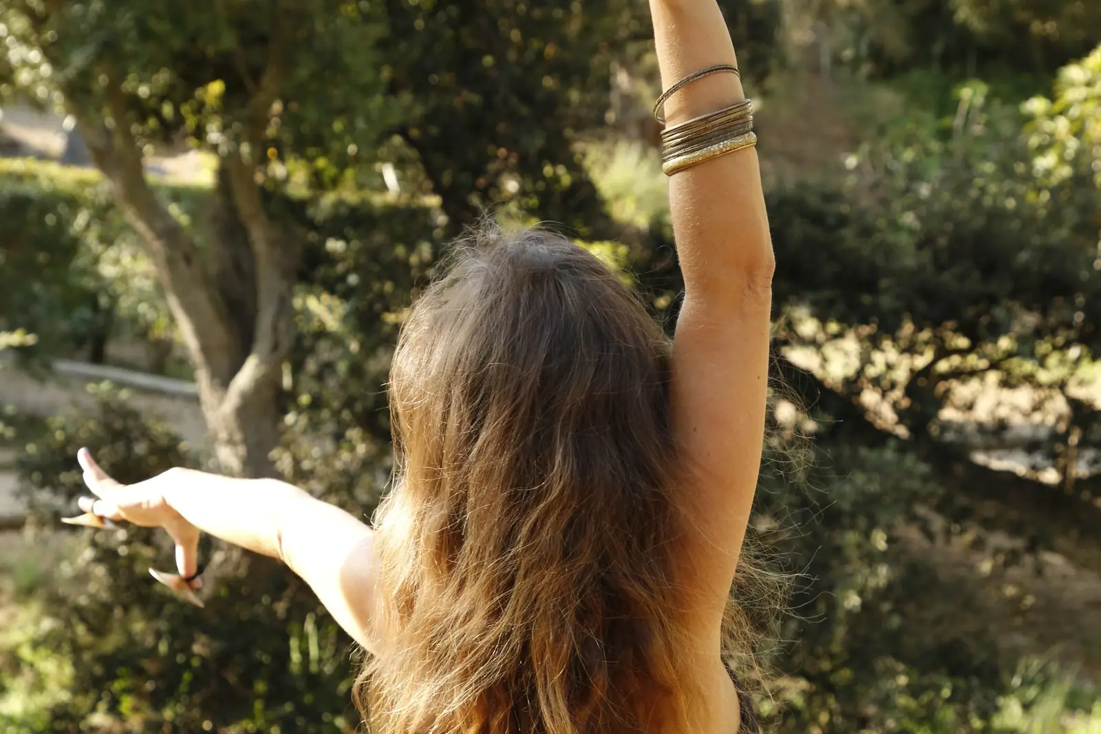 Ana de costas, de braços abertos com címbalos de dedo e o cabelo longo ao sol, junto a um lago com nenúfares
