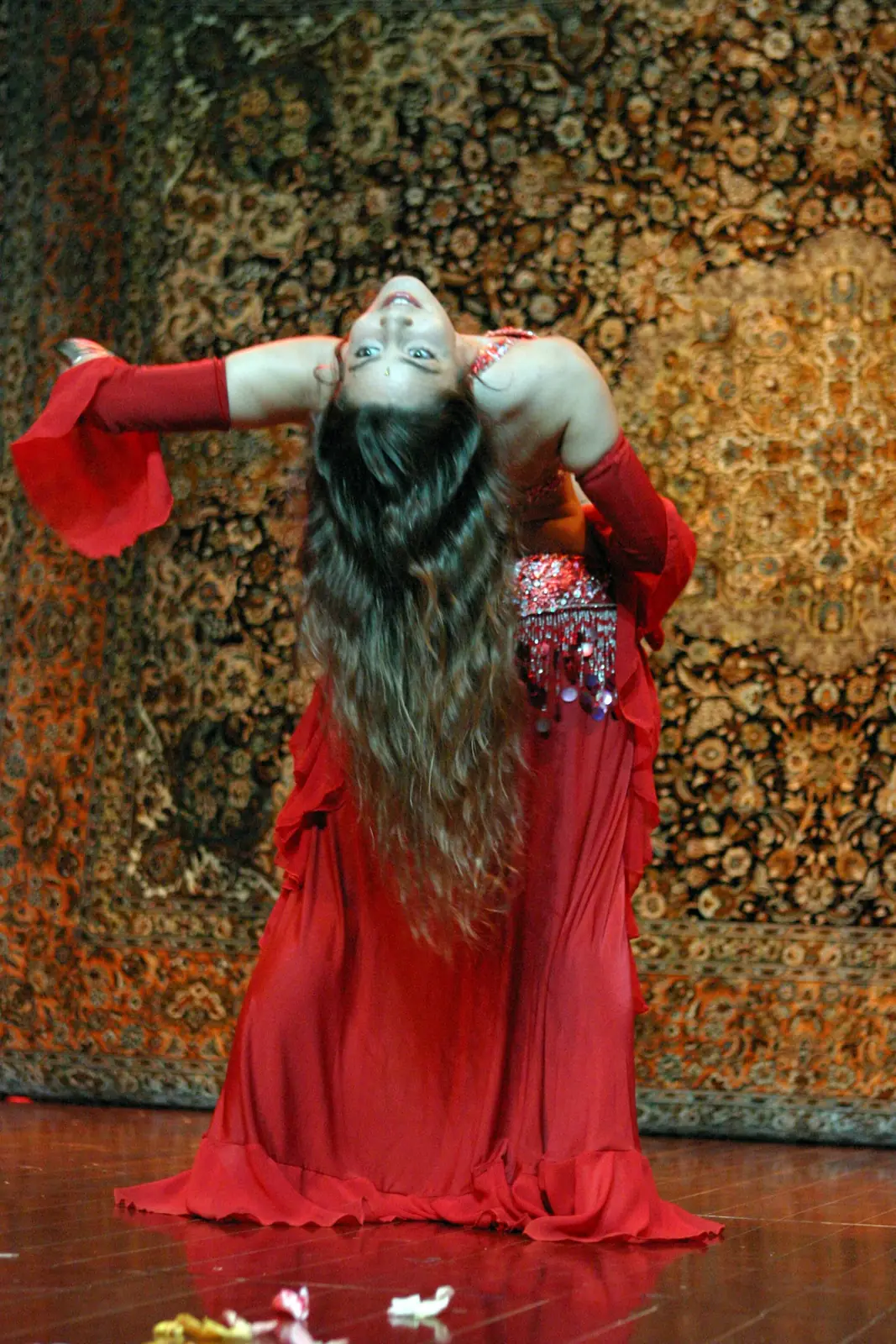 Ana num arco para trás em palco, de traje vermelho e cabelo comprido a cair, diante de um tapete oriental