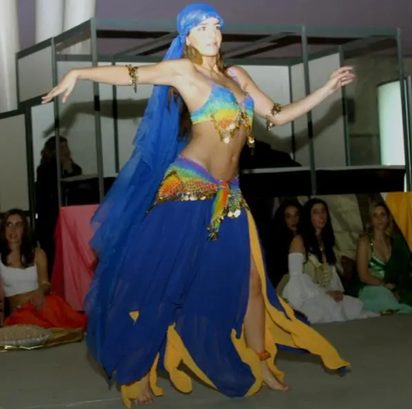 Ana dancing in a flowing blue and gold costume with arms opened wide