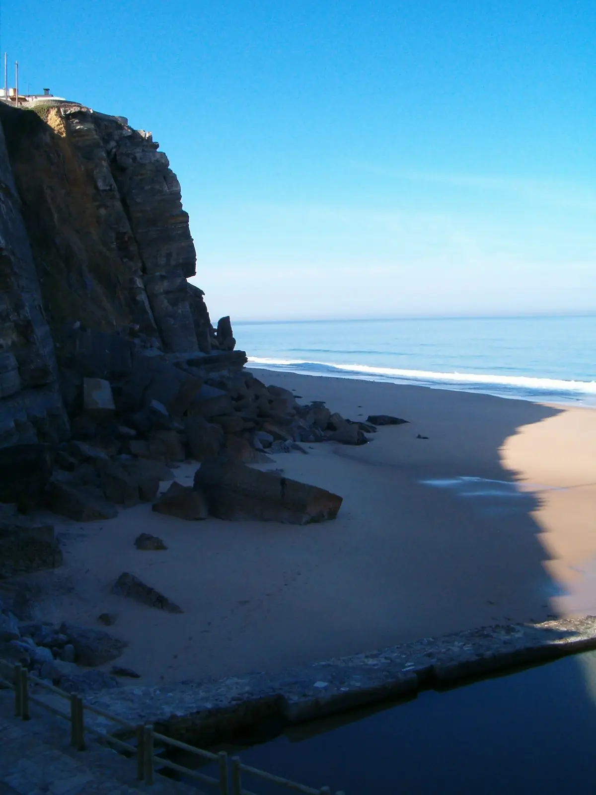 A rocky cliff above a sandy beach and a calm sea